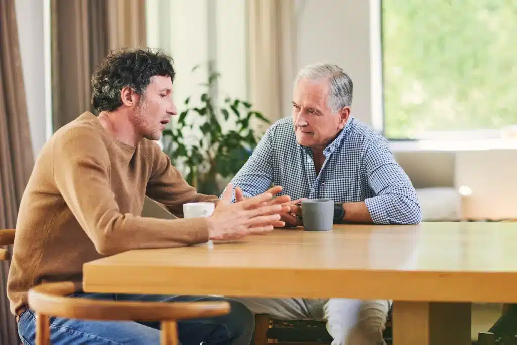 A man having a thoughtful conversation with an older adult at a table, discussing important family decisions