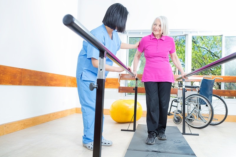 Outpatient therapy staff assisting senior with walking exercises in Lewisville, TX
