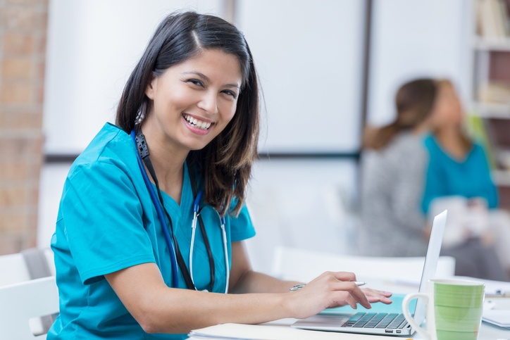 Nurse smiles while typing on laptop at nurse station in Lewisville, TX